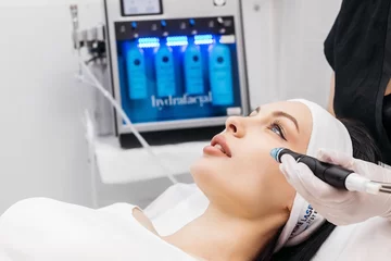 Vlies Fototapete Schönheitssalon Cosmetology clinic. Professional female cosmetologist doing hydrafacial procedure while being a work. Attractive nice woman lying on the medical bed while having beauty procedures