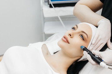 Fototapeta premium Cosmetology clinic. Professional female cosmetologist doing hydrafacial procedure while being a work. Attractive nice woman lying on the medical bed while having beauty procedures