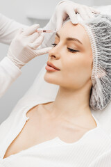 Skin lifting injection. A young woman is receiving a Botox injection in her forehead while lying on a white background. The concept of prolonging youth and cosmetology