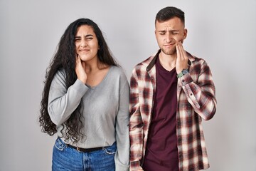 Young hispanic couple standing over white background touching mouth with hand with painful expression because of toothache or dental illness on teeth. dentist