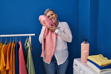 Middle age woman smiling confident touching soft sweater with face at laundry room