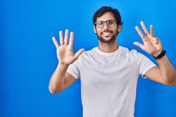 Naklejka premium Handsome latin man standing over blue background showing and pointing up with fingers number nine while smiling confident and happy.