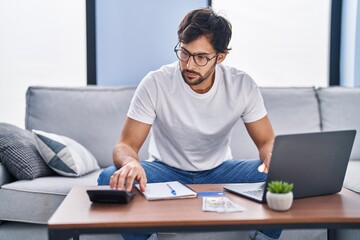 Young hispanic man using laptop working at home