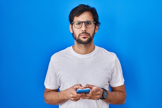 Handsome latin man using smartphone typing message skeptic and nervous, frowning upset because of problem. negative person.
