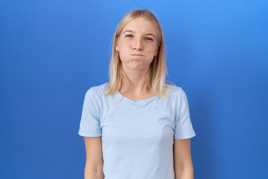 Young caucasian woman wearing casual blue t shirt puffing cheeks with funny face. mouth inflated with air, crazy expression.