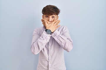 Arab man with beard standing over blue background shocked covering mouth with hands for mistake. secret concept.