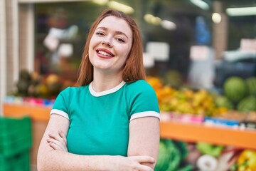 Young redhead woman standing with arms crossed gesture at street