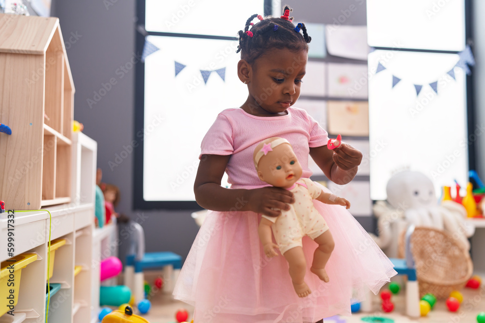 Wall mural African american girl holding baby doll standing at kindergarten