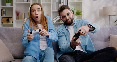 Happy adult man and woman playing enjoying video game and laughing together. Excited funny young adult couple gamers holding controllers playing video game at home.