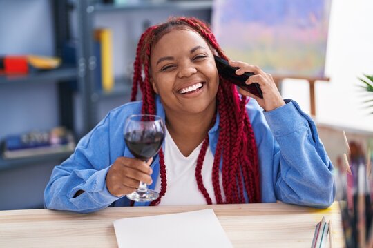 African american woman artist talking on smartphone drinking wine at art studio