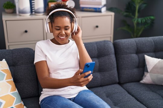 African american woman listening to music sitting on sofa at home
