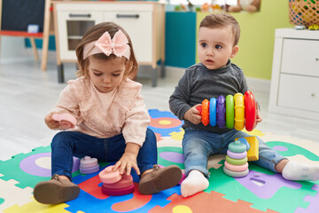 Adorable boy and girl playing with hoops game sitting on floor at kindergarten