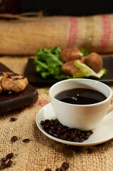 Cup of coffee, coffee beans and sweet bread, placed in a sack.