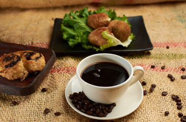 Cup of coffee, coffee beans and sweet bread, placed in a sack.