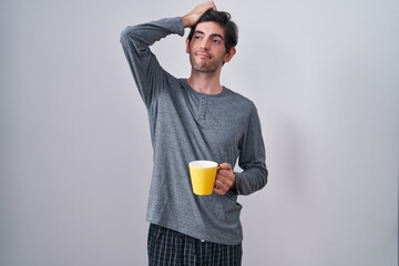 Young hispanic man wearing pajama drinking a cup of coffee confuse and wondering about question....
