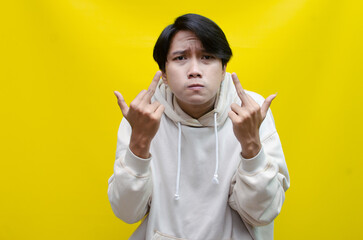 Asian young man showing his middle finger with a bad and angry expression isolated over a yellow...