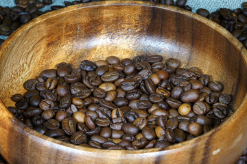Coffee beans in a round wooden bowl close-up. Roasted aromatic coffee macro. Brown coffee background