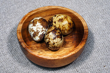 Quail eggs in a round wooden bowl on canvas, close-up, macro. Eggshell stains. Spotted pattern on the eggs. Dietary healthy foods. Egg
