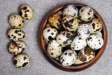 Quail eggs in a round wooden bowl on canvas, close-up, macro. Eggshell stains. Spotted pattern on...