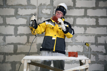 Locksmith in special clothes and goggles works in production. Worker. A man in a helmet and with a grinder in his hand. Industry. Builder. Metal processing with angle grinder