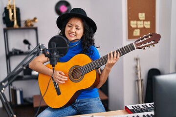 Fototapeta na wymiar Young chinese woman artist singing song playing guitar at music studio