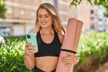 Young woman using smartphone holding yoga mat at park