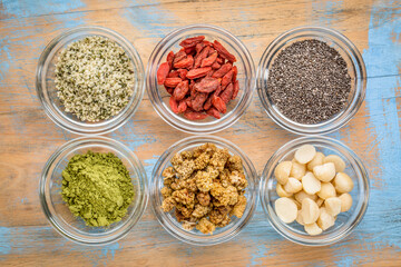superfood abstract - hemp seeds, goji berries, chia seeds, matcha tea powder, mulberries and macadamia nuts - top view of glass bowls on wood