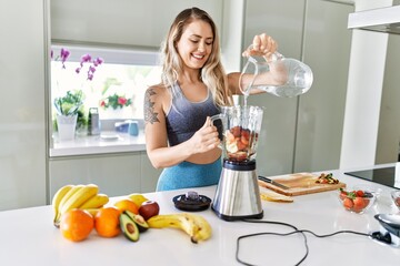 Young woman smiling confident pouring water on blender at kitchen