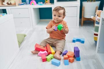 Adorable blond toddler playing with ball and geometry blocks sitting on floor at kindergarten