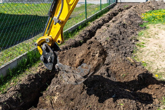 Mini digger digging a hole in the garden along the fence to the drainage pipes.