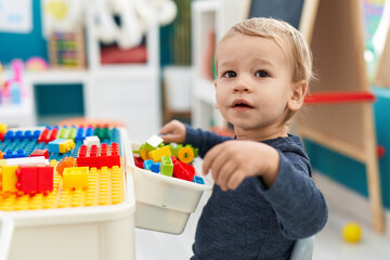 Adorable blond toddler playing with construction blocks standing at kindergarten