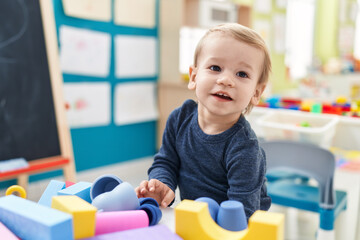 Fototapeta na wymiar Adorable blond toddler playing with geometry blocks standing at kindergarten