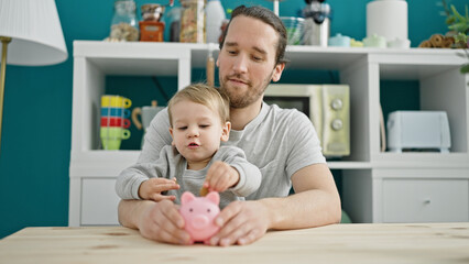Father and son inserting coin on piggy bank sitting on table at dinning room