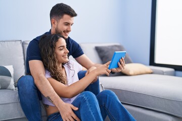Obraz premium Young hispanic couple using touchpad sitting on sofa at home