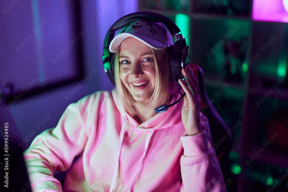 Wall mural Young blonde woman streamer smiling confident wearing headphones at gaming room