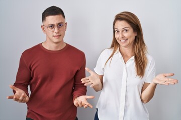 Mother and son standing together over isolated background clueless and confused with open arms, no idea concept.