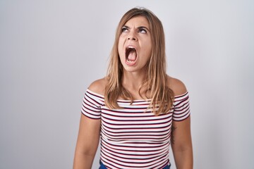 Young hispanic woman standing over isolated background angry and mad screaming frustrated and furious, shouting with anger. rage and aggressive concept.