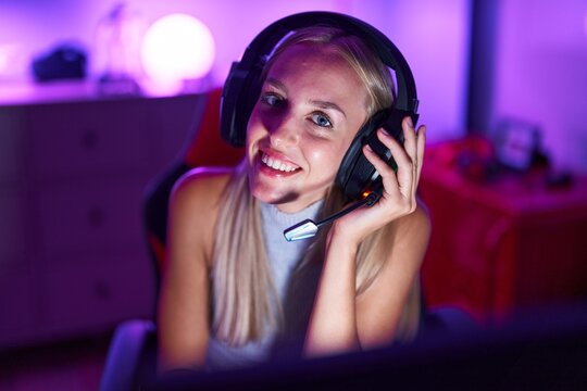 Young blonde woman streamer smiling confident sitting on table at gaming room