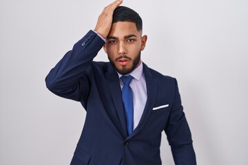 Young hispanic man wearing business suit and tie surprised with hand on head for mistake, remember error. forgot, bad memory concept.