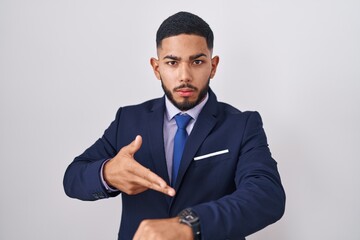 Young hispanic man wearing business suit and tie in hurry pointing to watch time, impatience, upset...