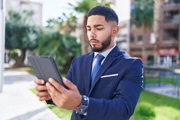 Young latin man business worker using touchpad with serious expression at park