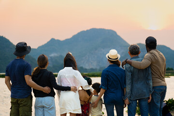 back view of happy family standing and looking at sunset behind the mountain and river beauty in...