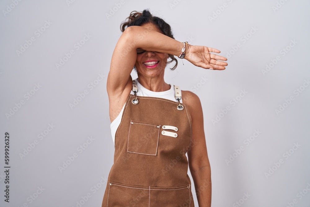 Sticker middle age woman wearing apron over white background covering eyes with arm smiling cheerful and fun