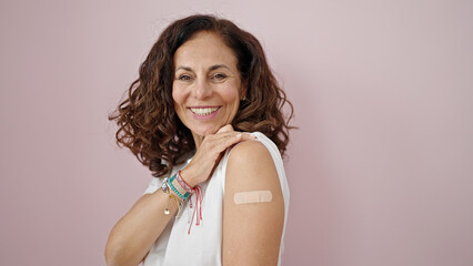 Middle age hispanic woman smiling confident standing with band aid on arm over isolated pink...