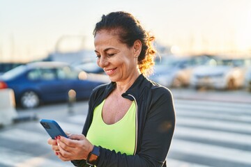 Middle age hispanic woman working out with smartphone outdoors