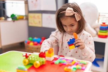 Adorable hispanic girl playing with construction blocks sitting on table at kindergarten