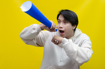 Shocked and surprised asian man shouting through paper megaphone giving an announcement.