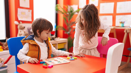 Adorable boy and girl playing with maths puzzle game sitting on table at kindergarten