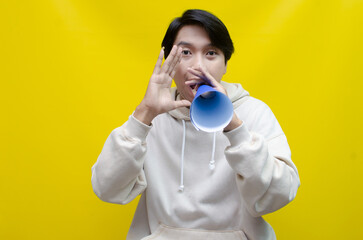 Shocked and surprised asian man shouting through paper megaphone giving an announcement.