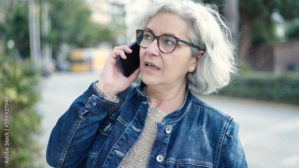 Poster Middle age woman with grey hair speaking on the phone at park